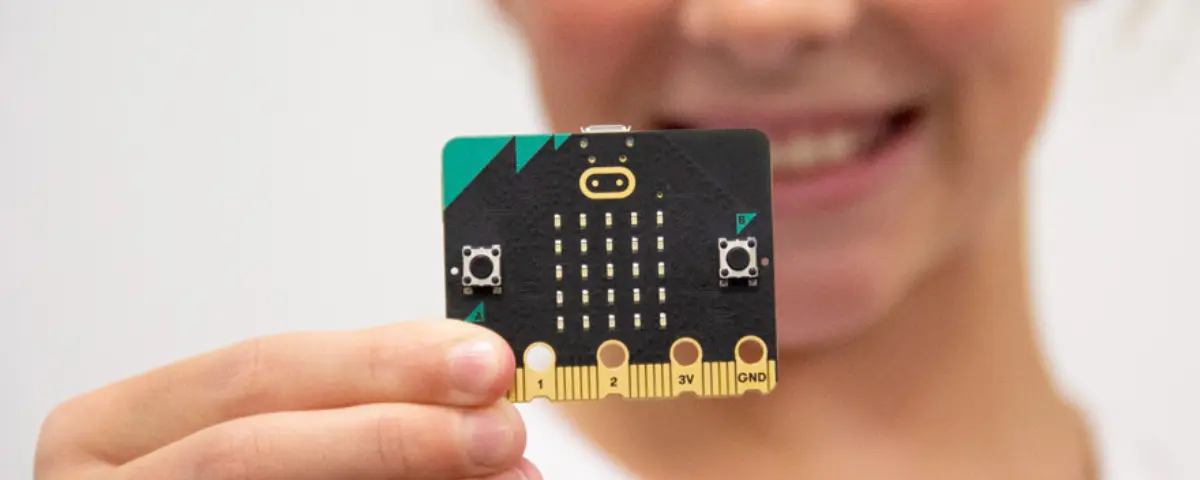 Student holding a micro:bit microcomputer and smiling. 