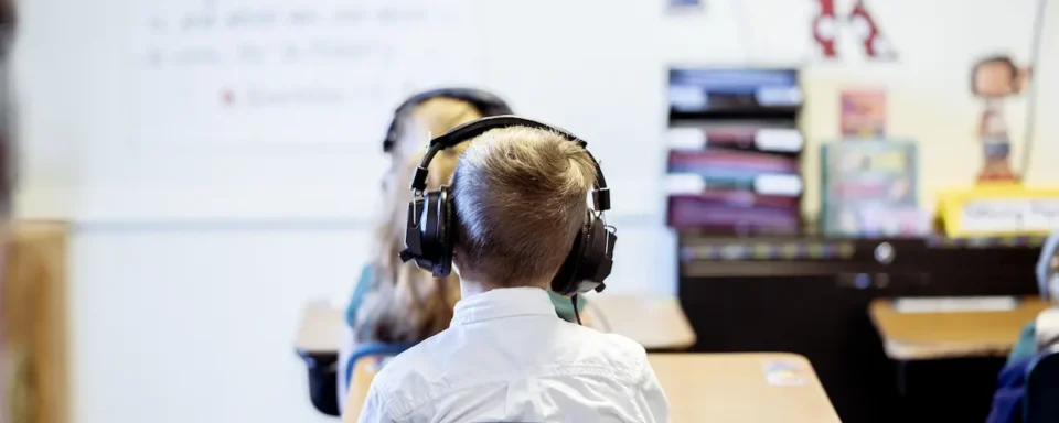A Student with headphones sits with his back to the camera, listening to a podcast to enhance STEM learning.