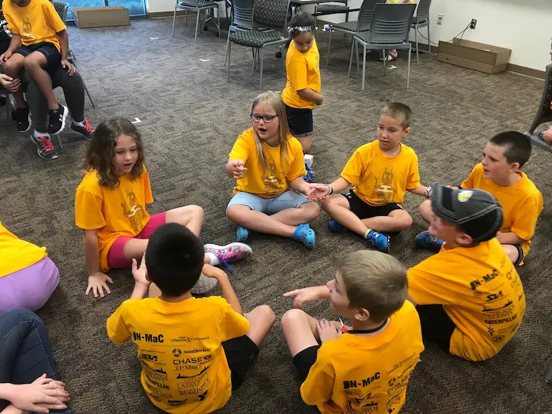 Kids sit in a circle to brainstorm solutions during a STEM summer camp
