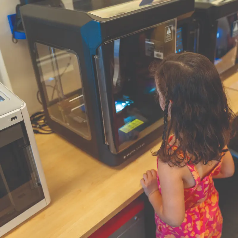 A little girl anxiously awaits the completion of her creation at a MakerBot 3D printer 