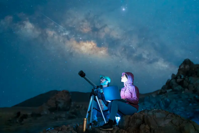 Couple sitting in the desert watching the stars and Milky Way next to a telescope