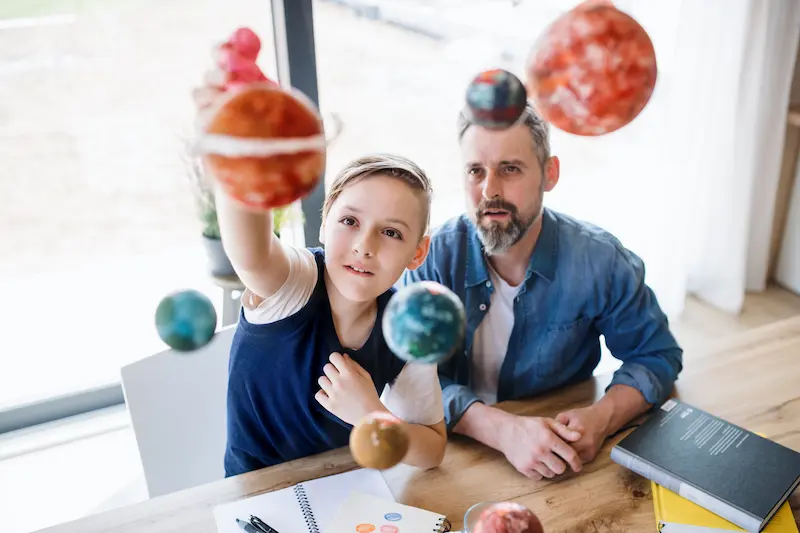 Mature father with small son sitting at table indoors, working on school project