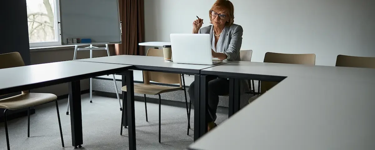 An educator sits in an empty classroom, searching for STEM education grants on her laptop.