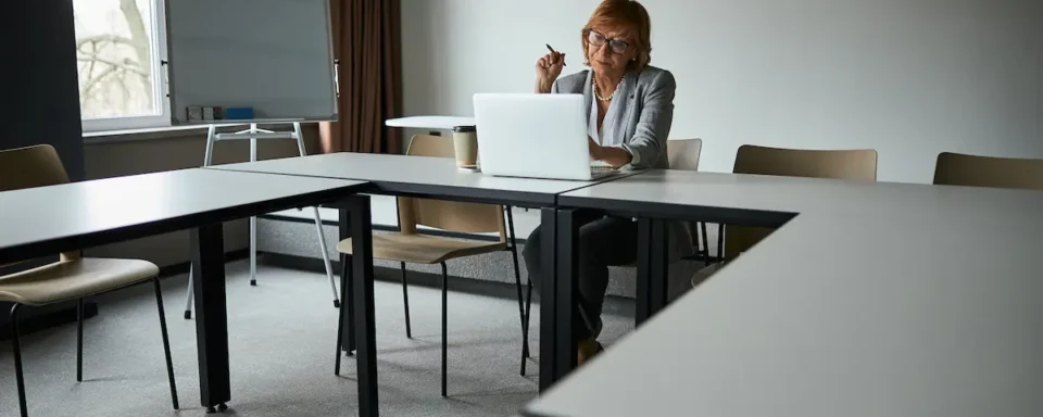 An educator sits in an empty classroom, searching for STEM education grants on her laptop.