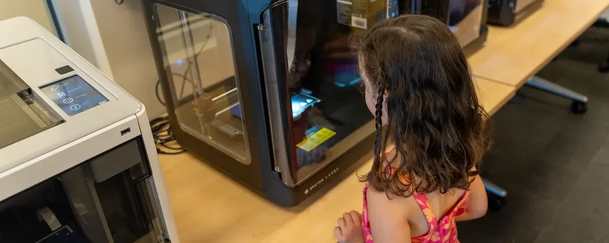 Female student awaits her creation during 3D printing in education.