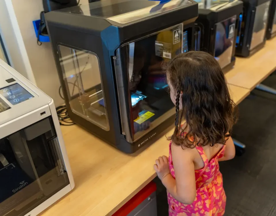 Female student awaits her creation during 3D printing in education.