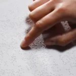 Child reading braille in a classroom.