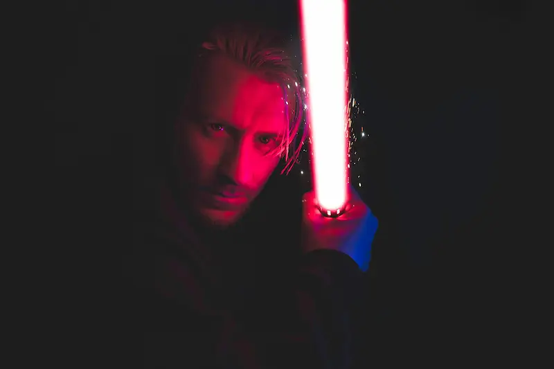 Man holding lightsaber with red light reflecting from his face