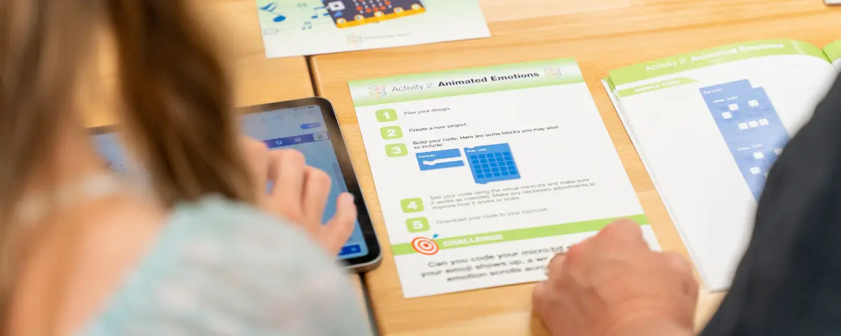 A student and a teacher working on micro:bit activity cards together.