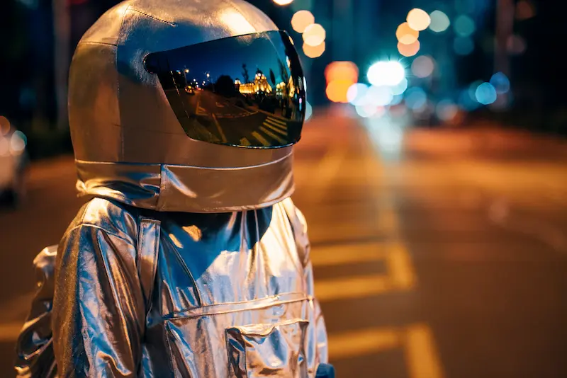 Spaceman in a silver suit on a city street at night.