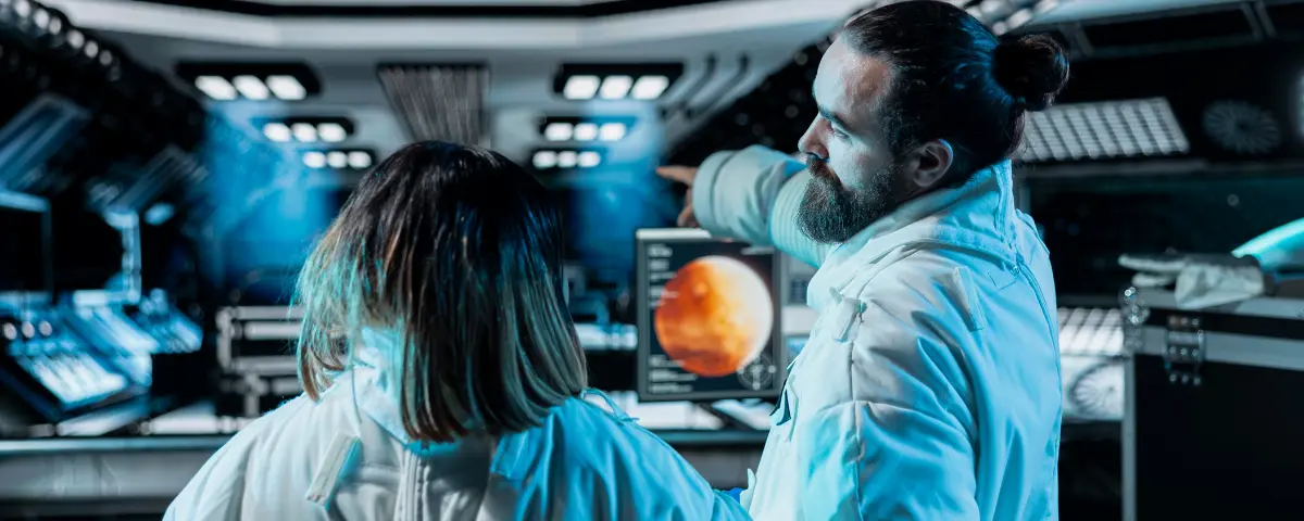 Two scientists stand in front of a control panel on a spaceship.