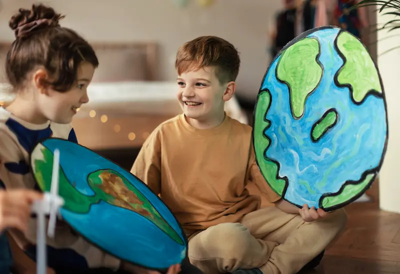 Smiling children holding up paintings of the earth.