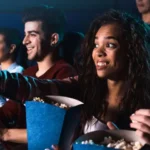 Group of cheerful people watching a movie in theaters while eating popcorn.