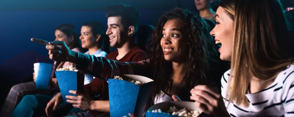 Group of cheerful people watching a movie in theaters while eating popcorn.
