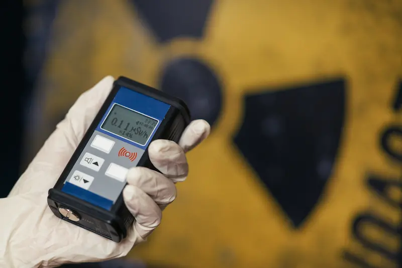 Scientist wearing gloves using a geiger counter to check radiation in front of a radiation warning sign. 