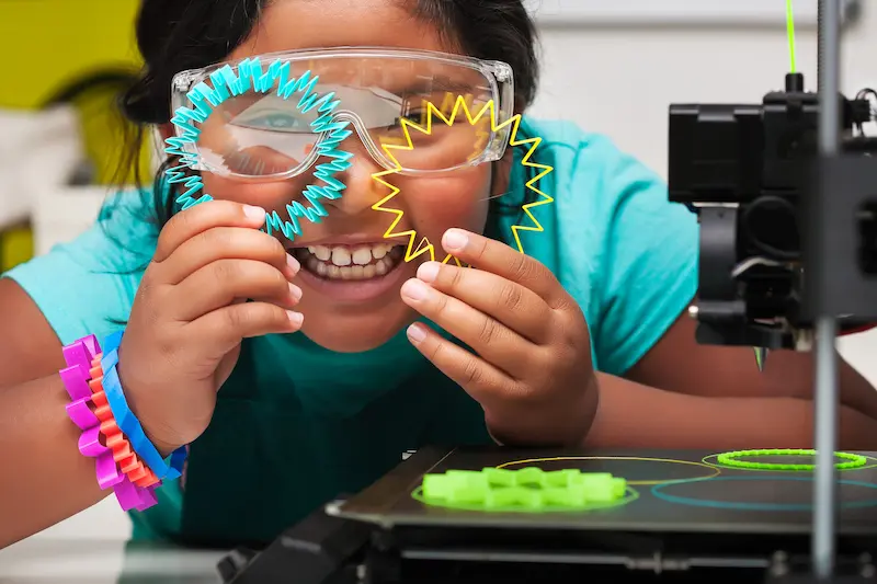 Smiling student holding up two brightly-colored, 3D-printed shapes.