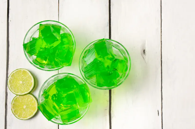 Lime gelatin squares in small bowls on a white background.