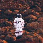 Astronaut standing on rocky terrain at sunset.