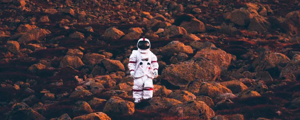 Astronaut standing on rocky terrain at sunset.