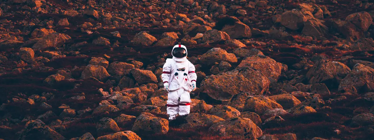 Astronaut standing on rocky terrain at sunset.