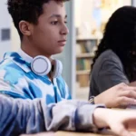 Four students working on laptops in a classroom.