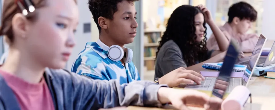 Four students working on laptops in a classroom.