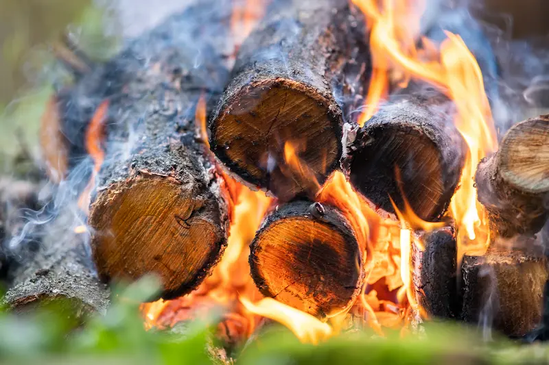 Close up of four logs in a pile burning brightly, releasing smoke.
