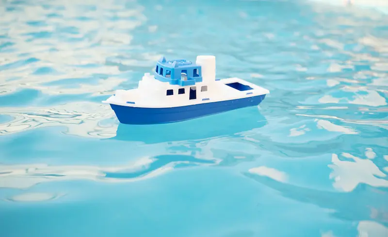 Blue and white toy ship floating in water from a pool.