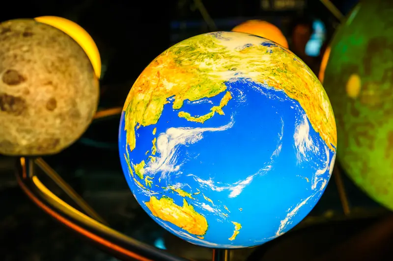 Colorful, illuminated model of the solar system, showing Earth and other planets orbiting around the Sun.
