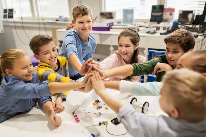 Group of students high-fiving around a table while working on a STEM project.