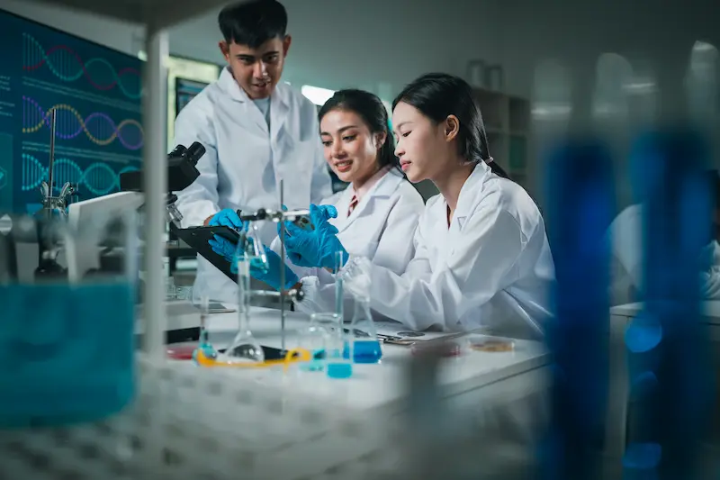 Two researchers wearing lab coats working in a laboratory holding beakers filled with liquids.