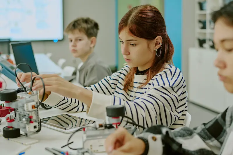 Three students working on a robotics project in a classroom.