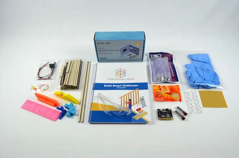 The Build Smart Clubhouse Kit with the curriculum booklet, wooden building pieces, micro:bit sensors, gloves, batteries, and other materials.