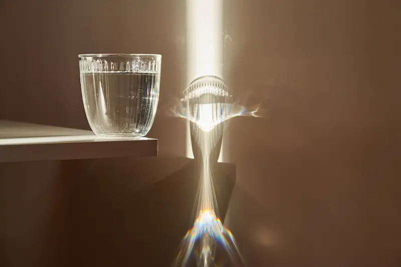 Light shining through a glass of water, causing refraction on the wall behind the glass.