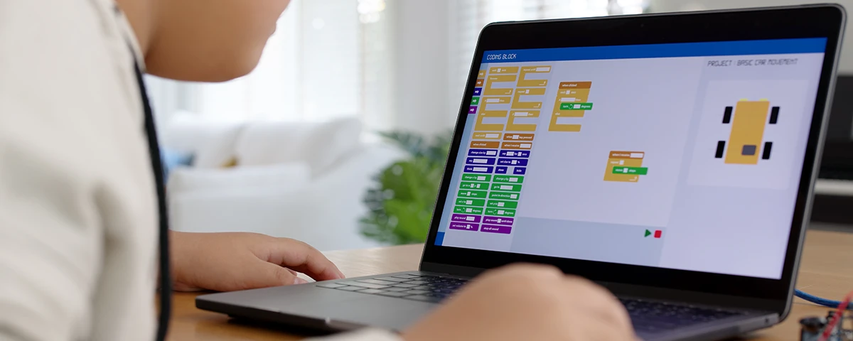 Child learning programming using block coding on a laptop.