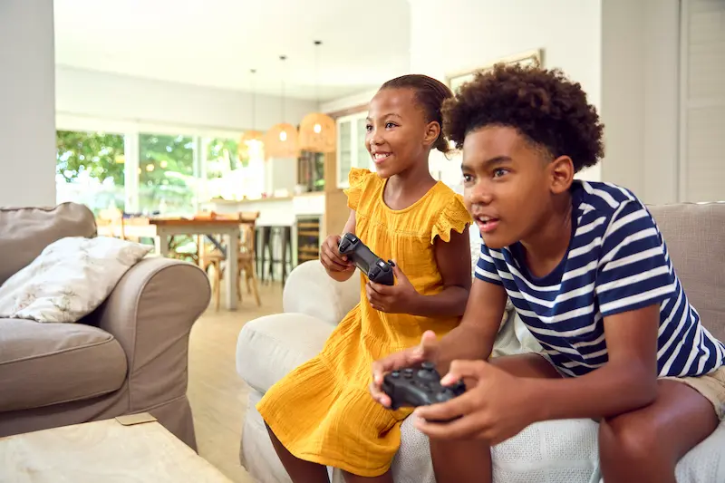 Two children playing video games on a couch in a living room.