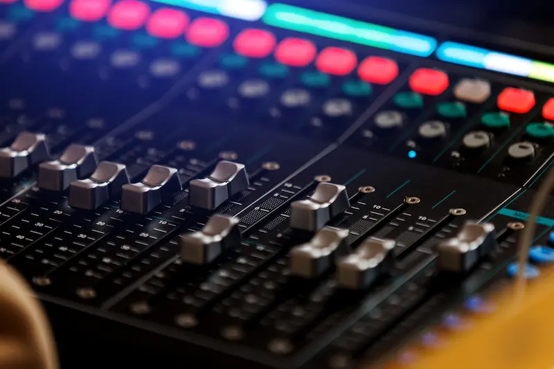 Sound mixing console with multiple volume sliders and other knobs to adjust audio.