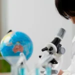Child wearing a white lab coat looking into a toy microscope.