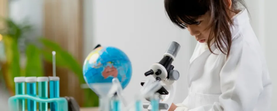Child wearing a white lab coat looking into a toy microscope.