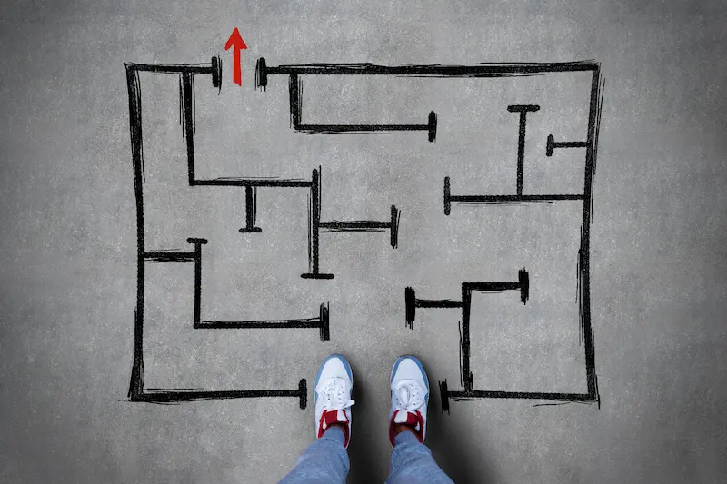 A person stands at the beginning of a simple maze painted onto a concrete surface.