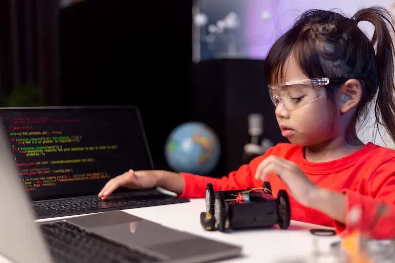 Girl programming a small, toy car by typing on a laptop.