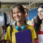 Group of smiling middle school students in a school hallway holding folders.