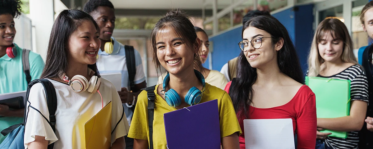 Group of smiling middle school students in a school hallway holding folders.