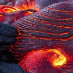 Close up of molten lava flowing over hardened black rocks.