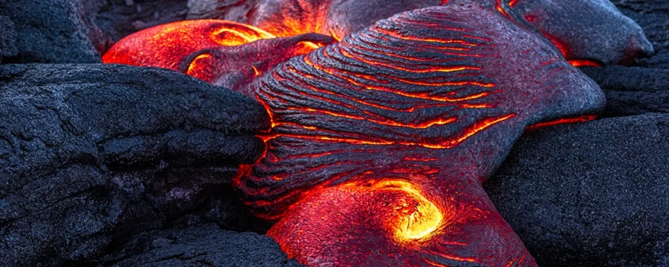 Close up of molten lava flowing over hardened black rocks.