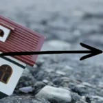 Small toy house sinking into a cracked asphalt road.
