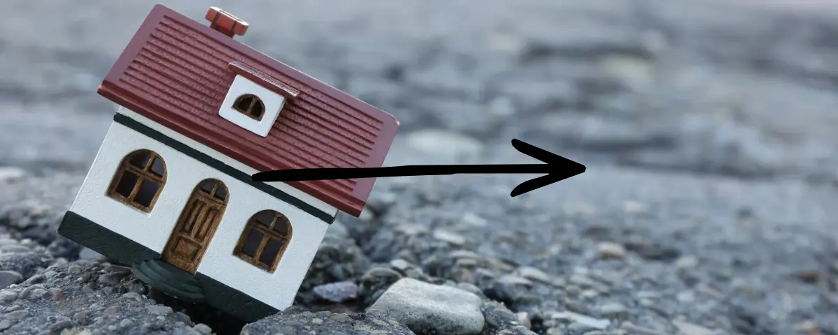 Small toy house sinking into a cracked asphalt road.