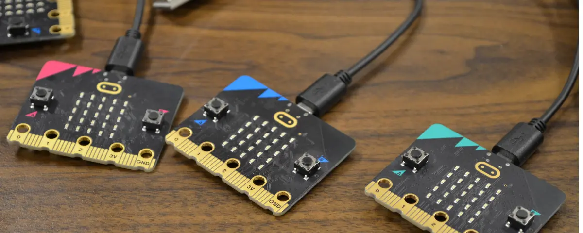 Three micro:bits attached to USB charging cables on a table.