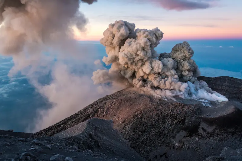 Scenic view of smoke going out of a volcanic mountain during sunset.