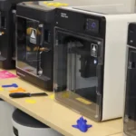 Several 3D printers on a table in a STEM classroom.